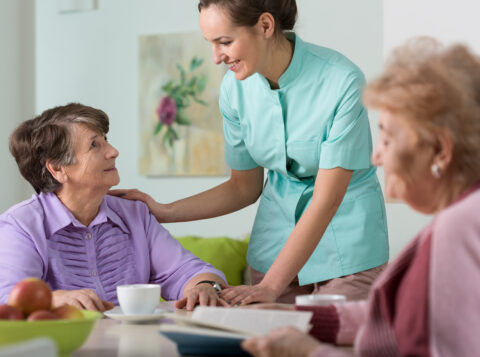 two women in assisted living talking with their nursing aid at table